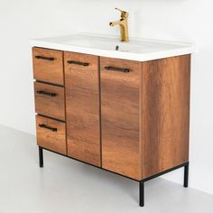 a bathroom vanity with a wooden cabinet and white counter top that has a gold faucet on it