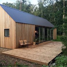 a wooden deck with two chairs on it next to a small house in the woods