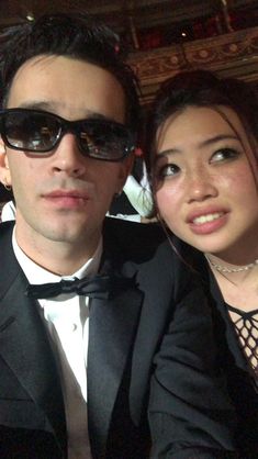 a man in a tuxedo poses with a woman who is wearing sunglasses and a bow tie