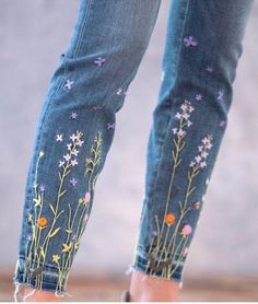 the legs of a woman wearing jeans with flowers painted on them are shown in front of a concrete wall