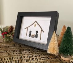 two small christmas trees are sitting next to a framed print with a family's house on it