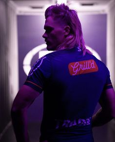 a man standing in front of a doorway with his back turned to the camera, wearing a purple shirt