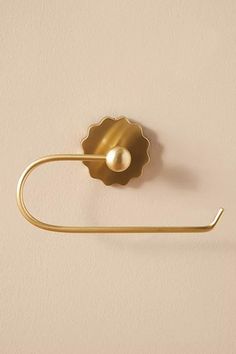 a gold towel ring with a pearl in the center on a white wall behind it