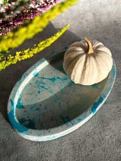 a white pumpkin sitting on top of a blue plate next to purple and yellow flowers