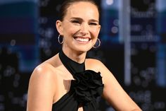 a smiling woman in a black dress with large hoop earrings on her head and one hand on her hip