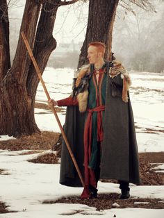 a man dressed in medieval clothing holding a stick and wearing a fur collared cape