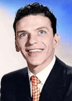 a man in a suit and tie smiling at the camera with blue eyes on his face