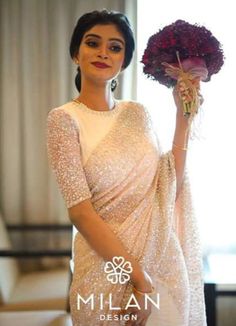 a woman in a white sari holding a bouquet of flowers on her left hand