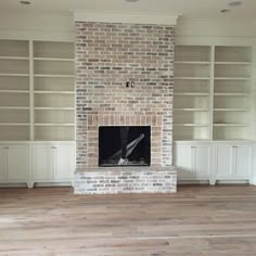 an empty living room with built - in bookcases and a brick fire place