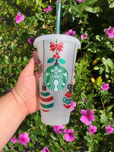 someone holding up a starbucks cup in front of some pink and purple flowers with a green straw