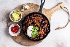 a skillet filled with beans, sour cream and other ingredients on a cutting board