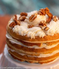 a stack of cake with white frosting and nuts on top sitting on a plate