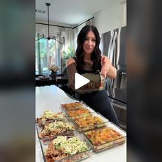 a woman standing in front of a table filled with trays of food and pointing to the camera