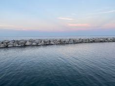 a long stone wall stretches out into the ocean at sunset or dawn, as seen from across the water