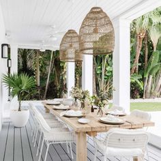 an outdoor dining area with white wicker chairs and wooden table