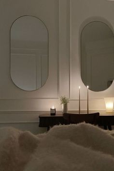 two round mirrors sitting on top of a wall next to a table with candles in it