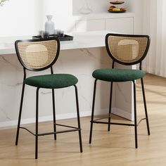 two green chairs sitting next to each other in front of a counter top with a vase on it