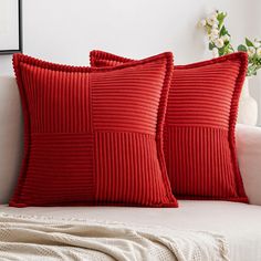 two red pillows sitting on top of a white couch next to a vase with flowers