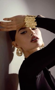 a woman in black shirt and gold earrings holding her hand up to her head with both hands