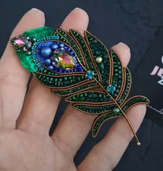 a hand holding a brooch with a leaf design on it's center piece