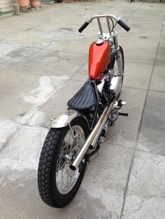 a red and black motorcycle parked on top of a cement floor next to potted plants