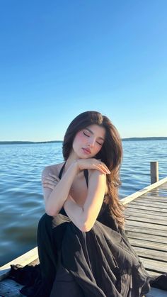 a woman sitting on top of a wooden pier next to the ocean with her arms crossed