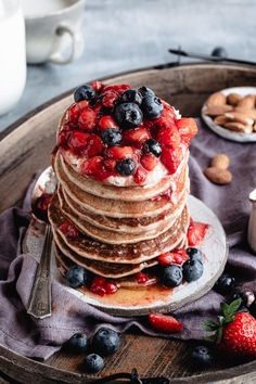 a stack of pancakes topped with berries and blueberries on top of a wooden tray