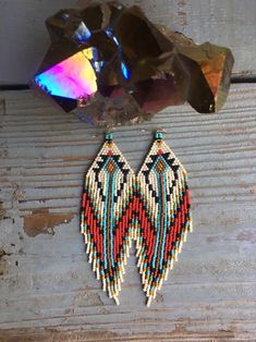 a pair of beaded earrings sitting on top of a piece of wood next to a rock