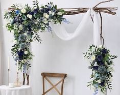 two white and blue flowers are hanging from a wedding arch with greenery on it