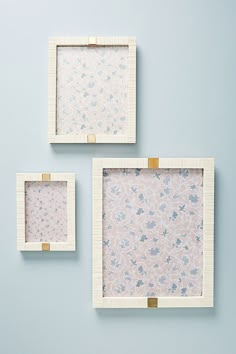 three square frames with flowers on them against a blue wall, one has gold trim and the other is white