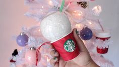 a hand holding a starbucks cup in front of a christmas tree with ornaments on it