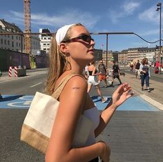 a woman walking down the street with her hand in her pocket while wearing sunglasses and carrying a tote bag