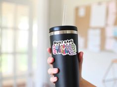 a woman holding a black tumbler with stickers on it's side that says quit game