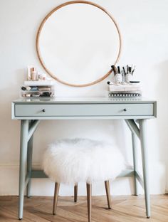 a blue desk with a round mirror above it and a white fur stool in front of it