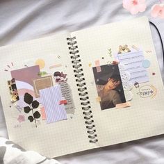 an open notebook with pictures and stickers on the pages, next to a pink flower