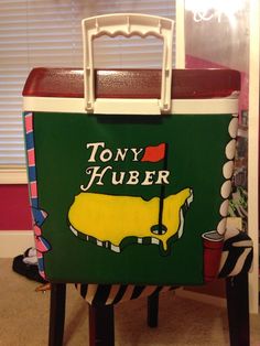 a cooler sitting on top of a wooden stool in front of a window with the words tony huber painted on it