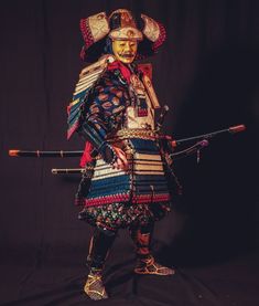 a man dressed in an elaborately designed costume and holding two swords, standing against a black background