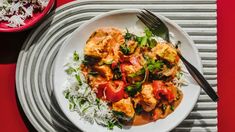 a white plate topped with rice and chicken next to a red bowl filled with vegetables