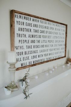 a white fireplace mantle with a wooden sign on it and candles in front of it