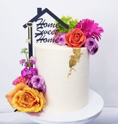 there is a white cake with flowers on the top and a house sign behind it