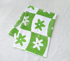 two green and white napkins with flowers on them sitting on a tablecloth covered surface