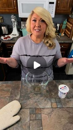 a woman standing in front of a kitchen counter holding her hands out to the camera