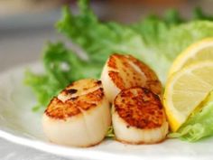 some scallops are sitting on a plate with lettuce and lemon wedges