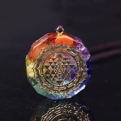 a colorful glass pendant with an intricate design on it's front end, sitting on a black surface