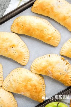 baked apple turnovers sitting on top of a baking sheet next to an apple slice