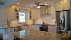 a kitchen with marble counter tops and stainless steel appliances, along with white cabinetry