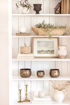 a white book shelf with vases and other items on it's top shelves