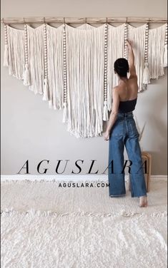 a woman standing on top of a bed in front of a wall hanging with tassels