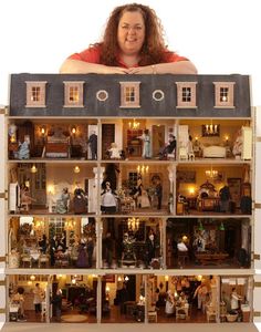 a woman is standing in front of a doll house with dolls on the top floor