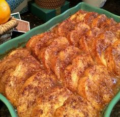 a green dish filled with cinnamon rolls on top of a counter next to oranges